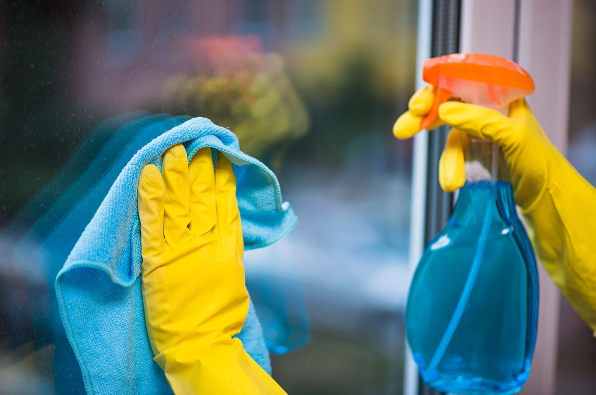A person wearing yellow latex gloves, cleaning a window with a cloth and cleaner.