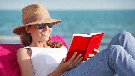 A woman reading a book on the beach knowing that she won't have to make a payment on her windows and doors for three months.