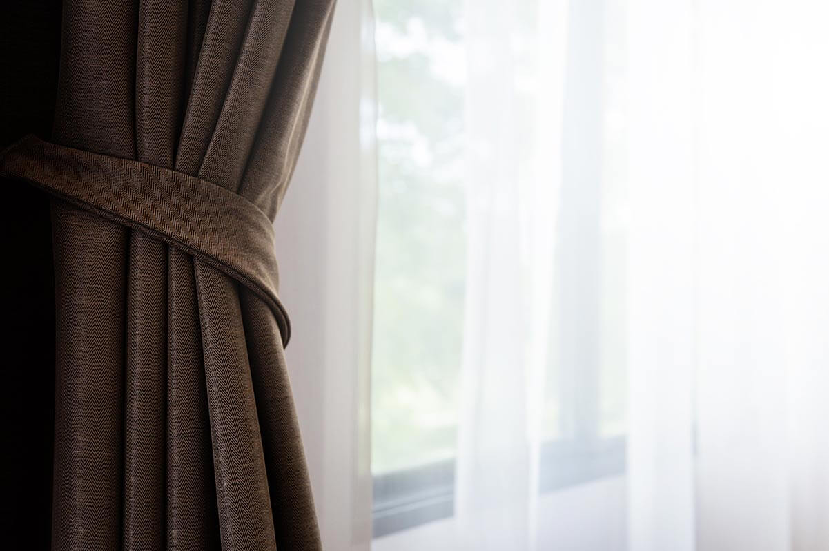 A brown curtain with a window in the background.