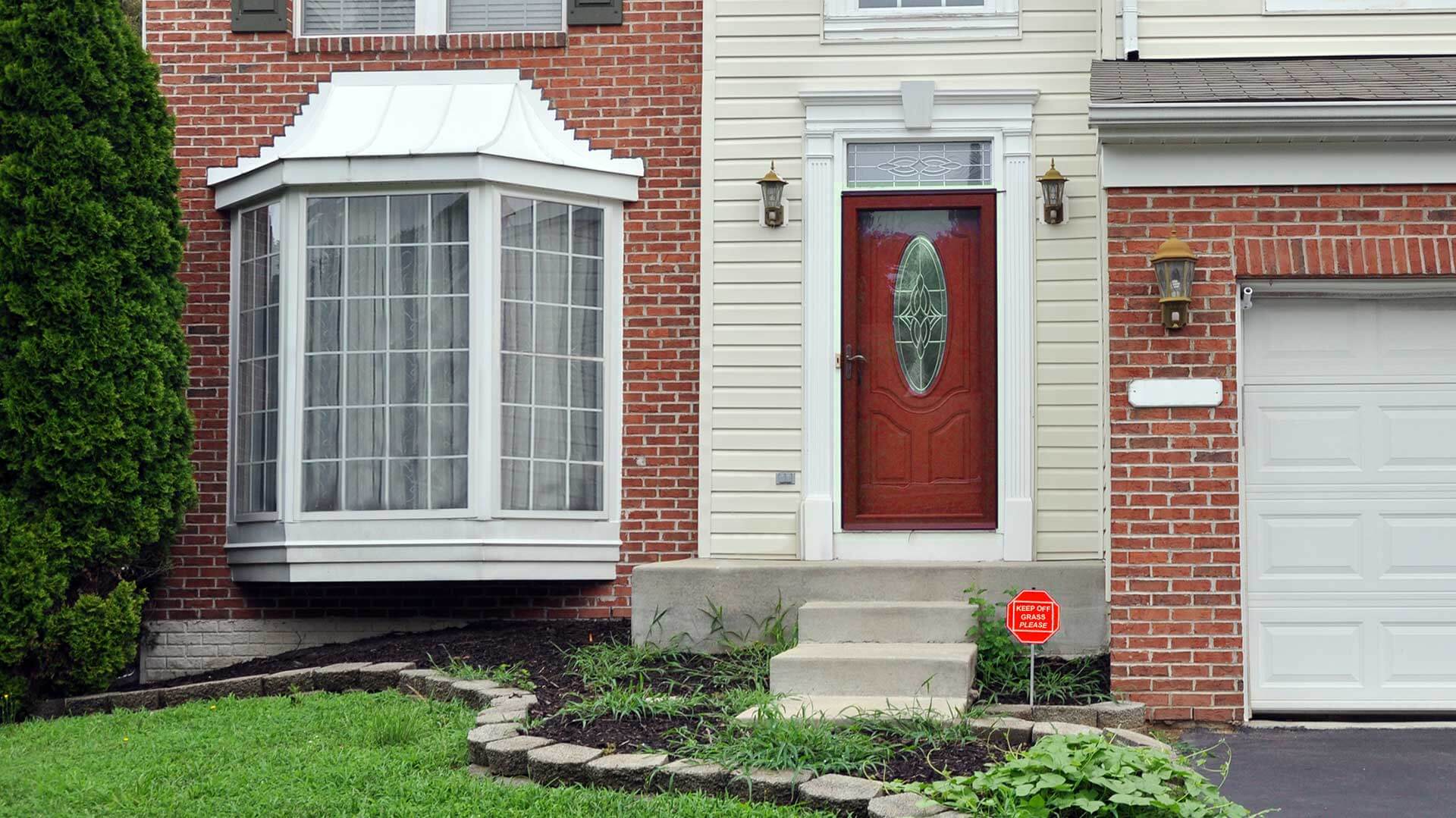 This detached house in red brick has a large bay window with colonial-style grilles, overlooking a landscaped front lawn and the driveway.