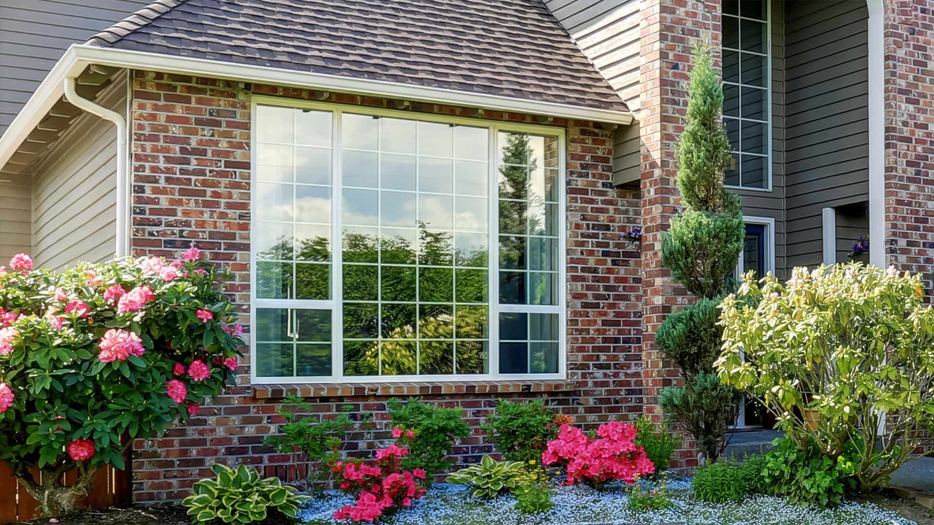 A red brick house with custom windows and a well maintained garden.