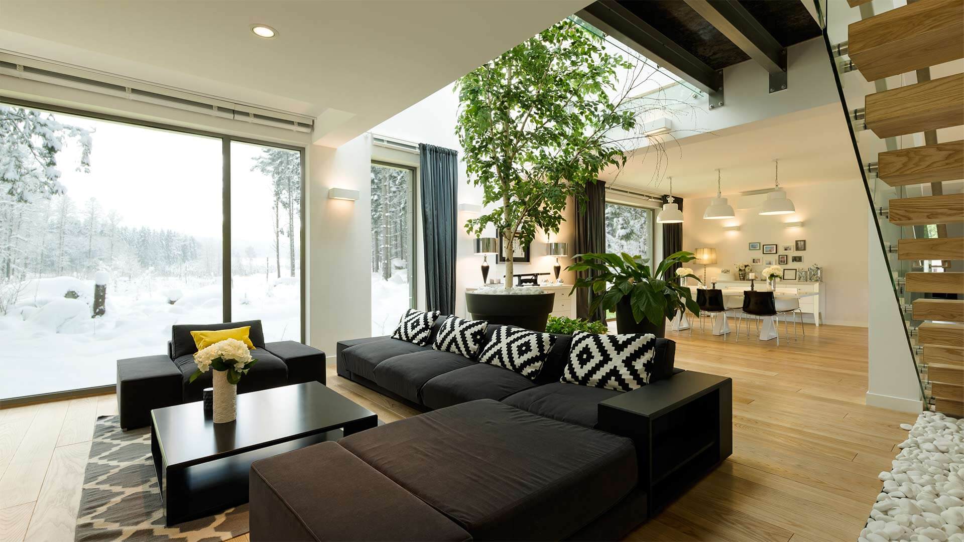 A modern home interior with plants, black sectional and Northern Comfort Patio Windows.
