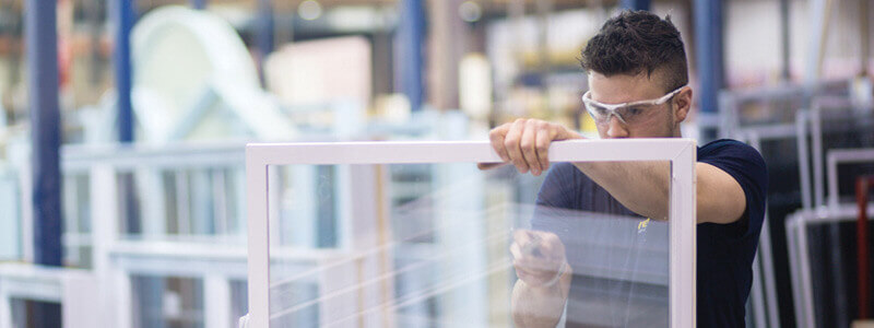 A young man cutting glass at the window manufacturing plant